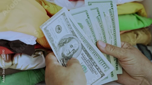 Close-up of hands counting dollar bills and hiding them among folded clothes in a closet. Concept of secret savings, financial security, privacy, and distrust in banks in a home setting.