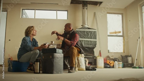 A middle-aged man and woman take a break in a home under renovation. They sit, eat, and discuss the project.