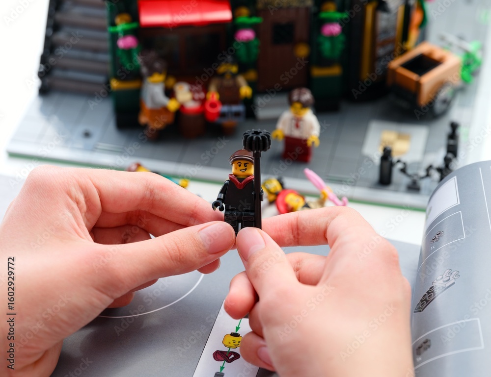 Obraz premium Tambov, Russian Federation - June 28, 2025 Person holding a built Lego chimney sweep minifigure on an instruction booklet. Lego set in the background