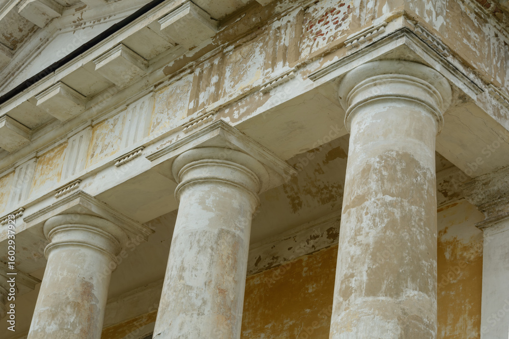 Three weathered neoclassical columns support an aged entablature, showing timeworn textures and fading paint on historic architecture. Three weathered neoclassical columns support an aged entablature, showing timeworn textures and fading paint on historic architecture.