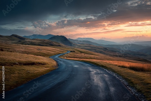 A road leading to the beautiful mountains of the Lake District in England, with a dramatic sky and sunset. 