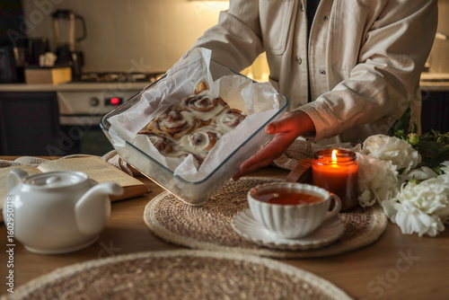 Billede på lærred Person holding a glass baking dish with freshly baked cinnamon rolls covered in icing