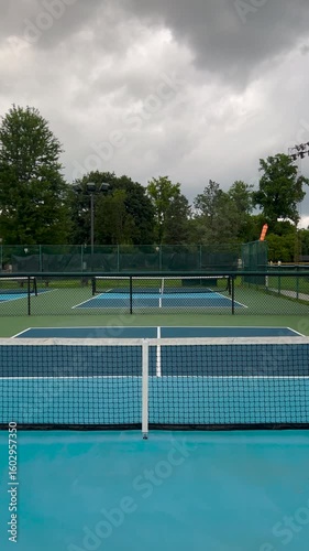 Wallpaper Mural Outdoor Pickleball Courts. Player point of view, moving forward across a pickleball court. Centerline view, looking towards the net. Public city park setting with cloudy blue Summer sky. Torontodigital.ca