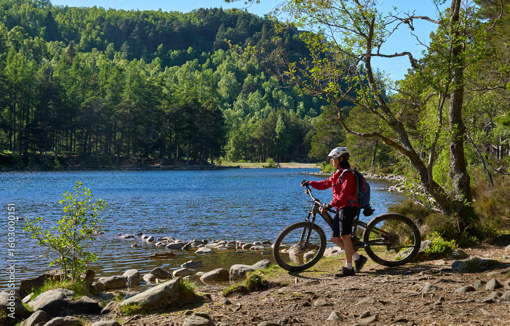 Fototapeta premium nice senior woman riding her electric mountain bike at Loch An Eilein in the Cairn Gorms National Park near Aviemore Scotland, UK