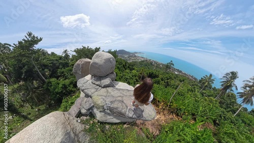 Woman Standing on Narrow Rock Edge Near Overlap Stone on Koh Samui with Vast Sea and Village Below Captured in Wide Angle Concept Extreme Nature Experience
