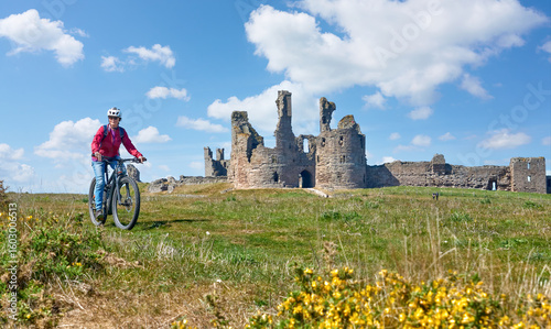 nice senior woman cycling with her elctric mountain bike at Dunstanburgh castle in north eastern England, UK