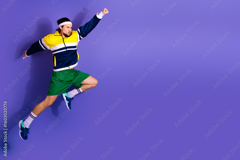 Obraz premium Energetic young man in colorful workout attire jumping against a vibrant purple background, exuding athletic energy