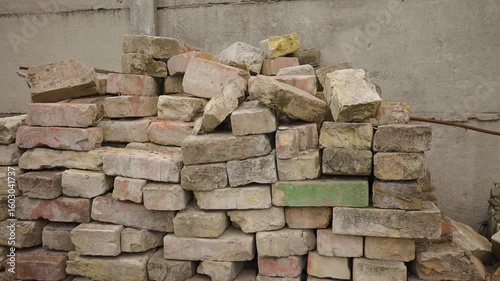 
Old bricks from a dismantled building lie stacked near a wall in the open air