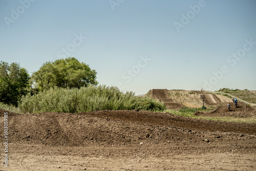 Motocross riders racing on a dirt track with large jumps and blue sky