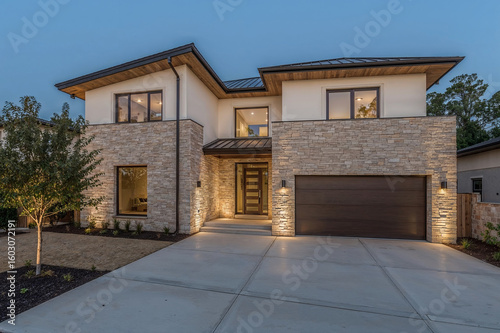 Modern luxury home with stone facade and garage at dusk