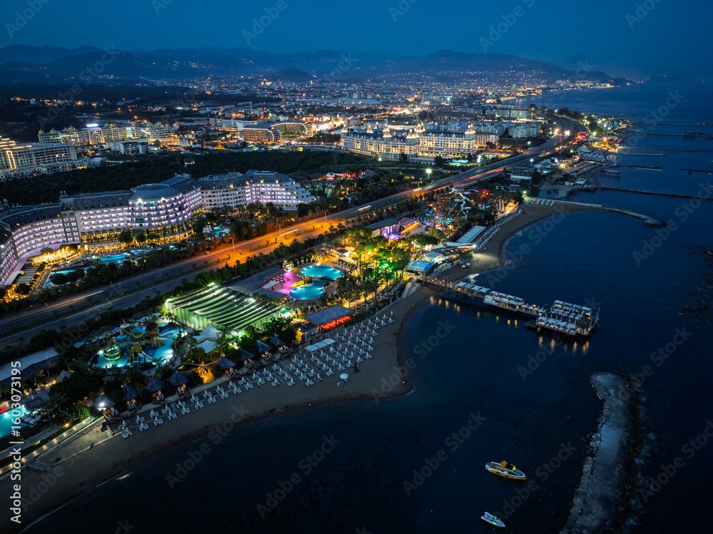 Fototapeta premium Stunning aerial sunset to night transition over Turkler in Alanya, Turkey. Alanya coastline,resorts,marina,hotels and city lights along the Mediterranean Sea drone view. Mediterranean Sea coastline.