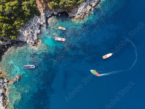 Fototapeta Naklejka Na Ścianę i Meble -  Aerial view of turquoise sea with boats near rocky coast and forest in Alanya, Turkey. Summer drone footage of scenic Mediterranean shoreline and clear water. Summer holiday in Alanya.