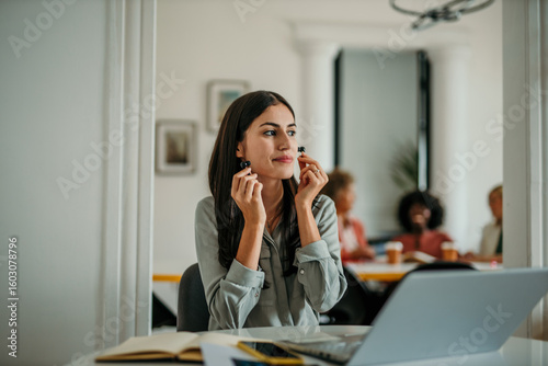 Businesswoman putting on wireless earphones at her desk in the office