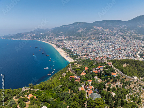Fototapeta Naklejka Na Ścianę i Meble -  Drone view of Alanya city, Turkey. Coastline, Mediterranean Sea, harbor, historic castle on the hill, and sprawling urban area with mountains in the background on a clear summer day. Alanya, Turkey