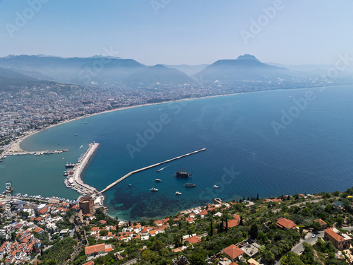 Fototapeta Naklejka Na Ścianę i Meble -  Drone view of Alanya city, Turkey. Coastline, Mediterranean Sea, harbor, historic castle on the hill, and sprawling urban area with mountains in the background on a clear summer day. Alanya, Turkey
