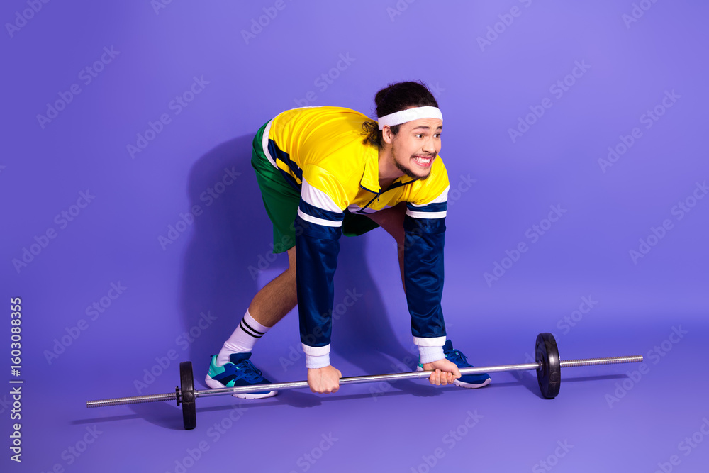 Naklejka premium Young male athlete lifting barbell in retro sportswear on vibrant purple background, showcasing fitness and vintage style