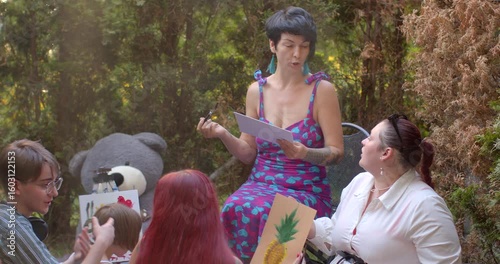 A group gathers in a serene park, engaging in lively discussions and sharing ideas. A woman presents information and later reads from a book, fostering collaboration and community interaction