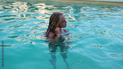 The child got water in his ear while swimming in the swimming pool. The girl cleans her ear from water.