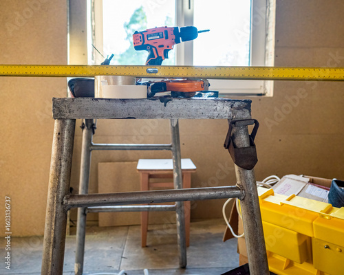 Construction tools arranged on a metal sawhorse. Renovation equipment, Drill and tape on stepladder