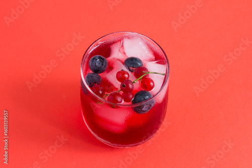 Cold lemonade or cocktail with red currants and blueberry in the drinking glass on a red background. Top view. Close-up.
