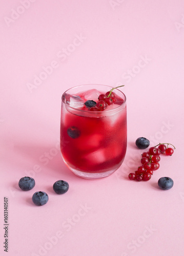 Cold lemonade or cocktail with red currants and blueberry in the drinking glass on a pink background. Location vertical.