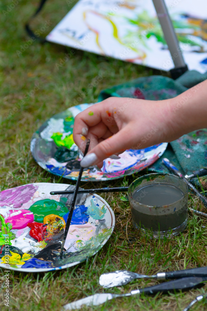 Obraz premium A person is artistically painting with a brush on a colorful palette while seated on the soft grass outdoors, enjoying the process