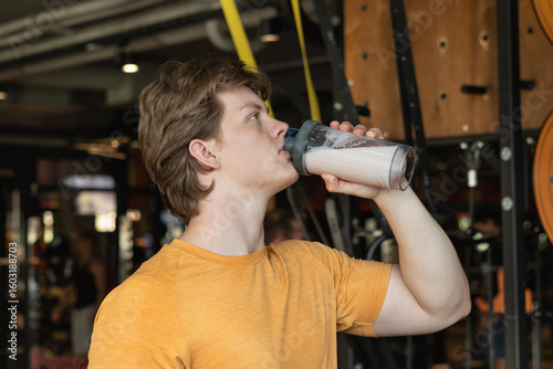 Bodybuilder or sporty young caucasian man drinking protein shake at gym. Working out.