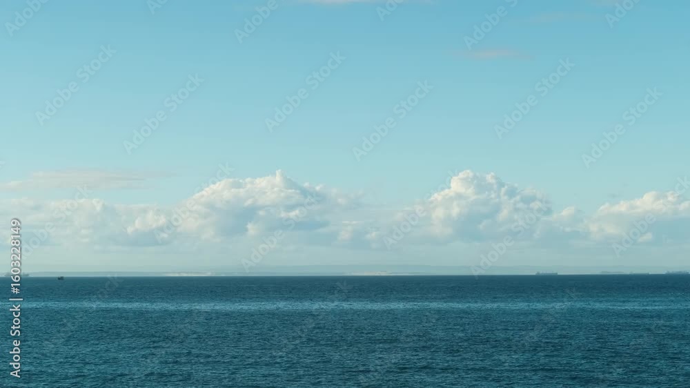 Timelapse of white cumulus clouds moving in overcast blue sky over a sea horizon during calm sunny day weather. Abstract aerial nature ocean sea and sky. Climate change, global warming concept