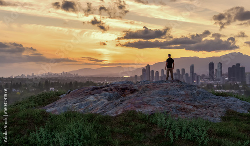 Man Watching Sunset Over Cityscape from Rocky Hilltop in Serene Landscape