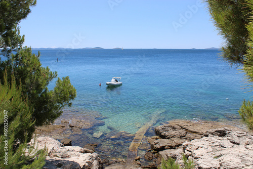 Boat on clear turquoise ocean water with rocky shore panorama horizon, Murter, Croatia