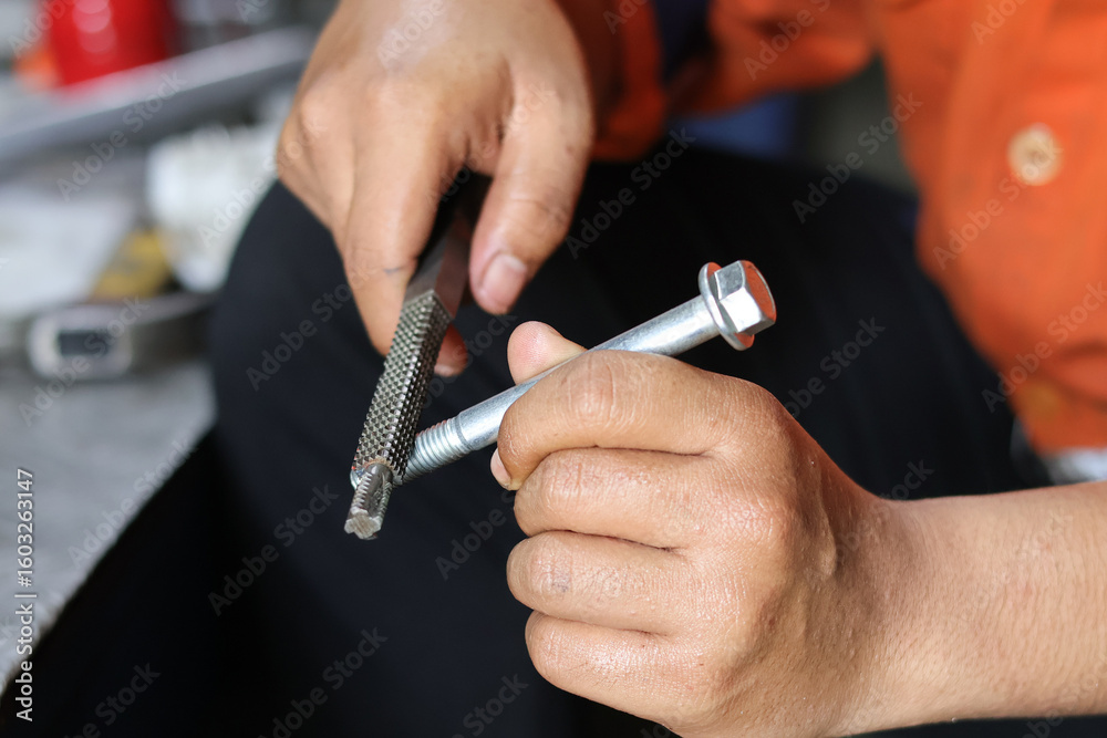 Fototapeta premium Close up of a hand cleaning a bolt thread using a thread file. Industrial concept.