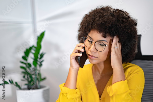Bild auf Leinwand Young Black woman in yellow shirt feeling stressed during a phone call in home office