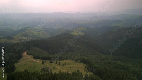 Flying over green forest at sunny summer day with the mountains on horizon with glowing clouds. Carpathian mountains, Europe