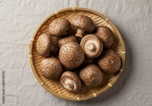 Fresh shiitake mushrooms with their textured caps facing upward, placed in a shallow bamboo basket on a clean linen cloth