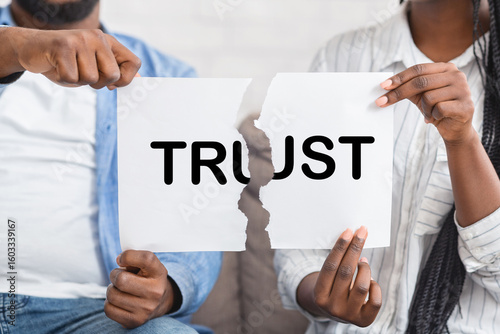 Mistrust concept. African american couple, man and woman, ripping paper with trust inscription.