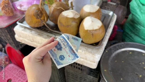 A tourist girl holds 25,000 Vietnamese dong in her hands and plans to buy a coconut at a local night market in Asia.