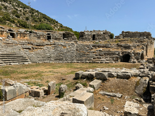 Ancient amphitheater ruins in a mountainous location during a clear day with blue sky