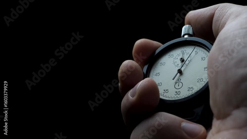 Male hand holds stopwatch and starts countdown. Second hand begins first tick. Concept of time control. Focus on precision and discipline. Dark background enhances intensity
