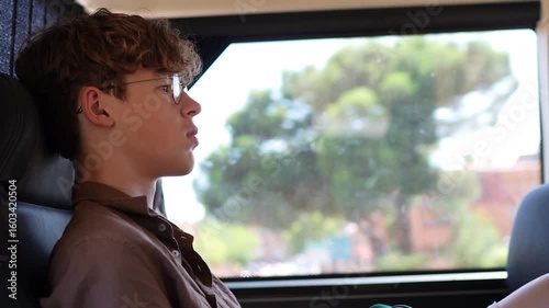 Wallpaper Mural Boy is seated on a bus, looking out the window, surrounded by soft natural light and greenery outside, capturing a moment of contemplation Torontodigital.ca