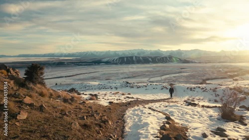 A man walks up a hill in the snowy mountains at sunset.
