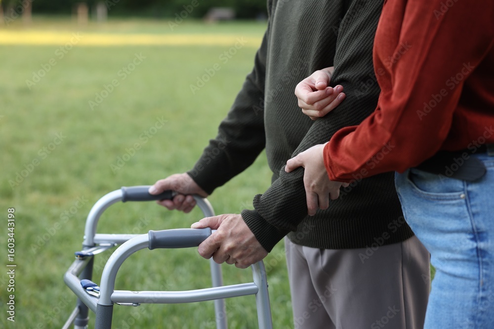Fototapeta premium Caregiver supporting elderly man who using walking frame outdoors, closeup