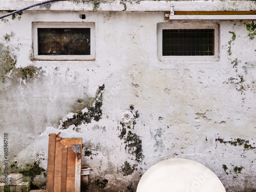 Fototapeta Naklejka Na Ścianę i Meble -  A street seasoned white  stained wall with two small windows and leftover materials on the floor