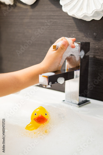 Boy in the sink playing with a rubber duck in the foam