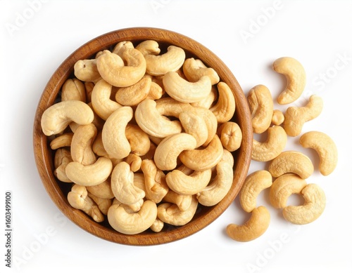 Top view of Roasted cashew nuts in wooden bowl with pile of cashew nuts on white background.