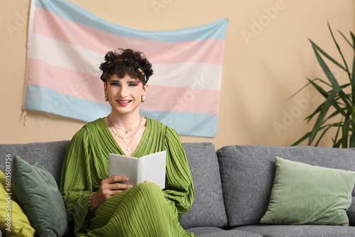 Foto Young transgender woman reading book on sofa at home