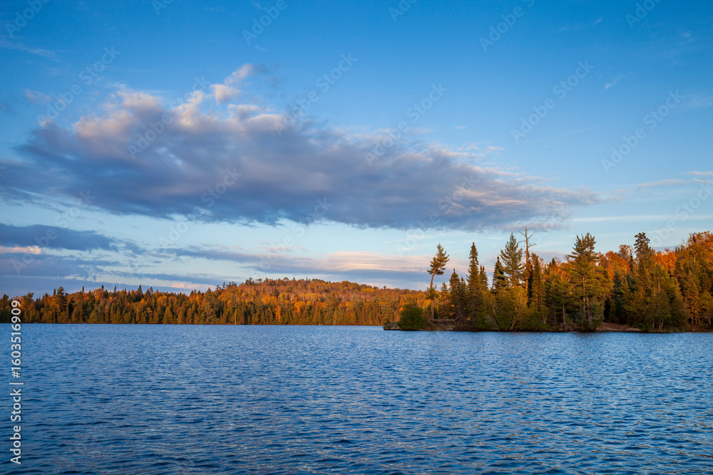 Fototapeta premium Blue trout lake with trees and hills in autumn color at sunset in northern Minnesota