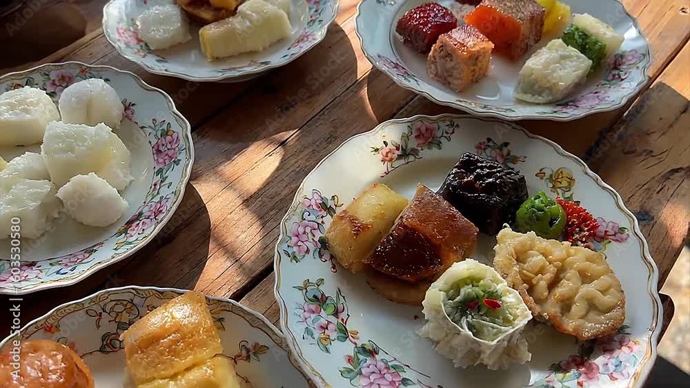 A vibrant arrangement of traditional Chinese desserts are presented on elegant floral-patterned plates atop a wooden table, showcasing a variety of shapes, textures, and colors for a visually delight
