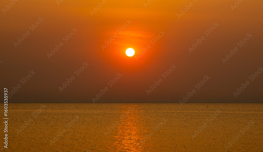 Obraz premium Beautiful photography view golden sun orang setting over calm sea, peaceful atmosphere and soft gradient sky create sense of serenity and timeless beauty perfect elaxation, travel, and nature