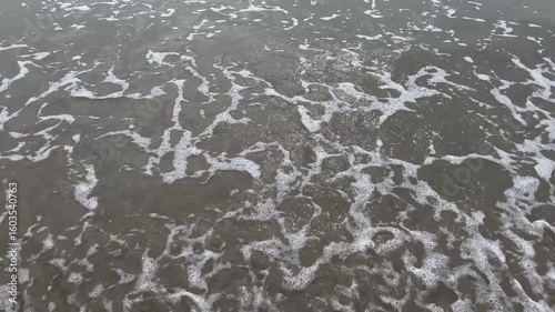 A close-up view of soft waves gently washing over a sandy beach, with delicate sea foam patterns forming on the surface