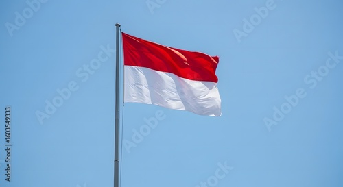 The Indonesian flag proudly waves against a bright, clear, and cloudless sky.